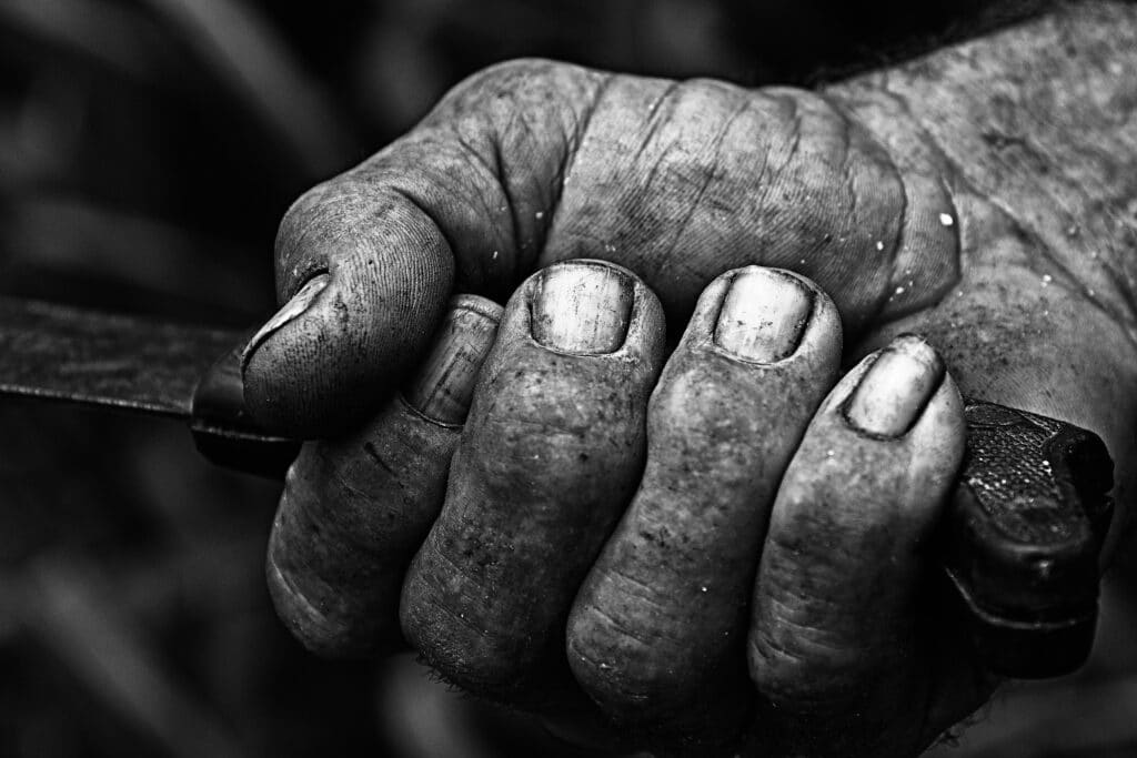 grayscale closeup shot of an old farmers dirty hand gripping a tool handle